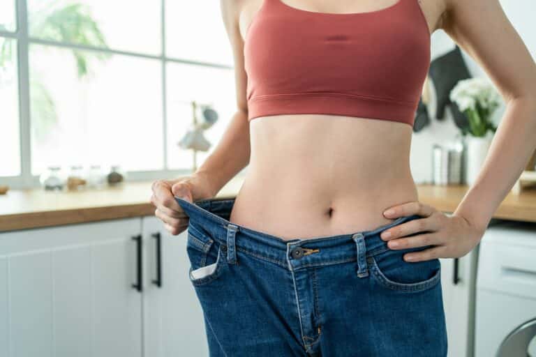 Close up of skinny woman wearing big jeans feeling happy after lose weight for health in house.